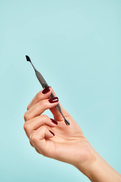 объект фото металлической кутикулы толкатель ногтей в руке молодой неизвестной женщины на ярком голубом фоне