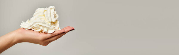 object photo of mouthwatering whipped cream in hand of unknown young woman on gray backdrop, banner