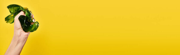 unknown young female model squeezing green jello in her hand on vibrant yellow backdrop, banner