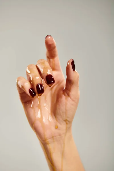 hand of unknown female model with nail polish covered with pure golden honey on gray background