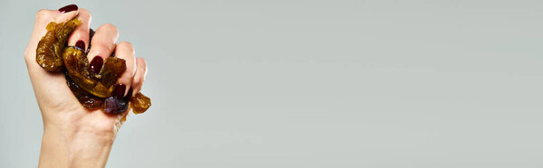 unknown woman with nail polish squeezing delicious juicy plum in her hand on gray background, banner