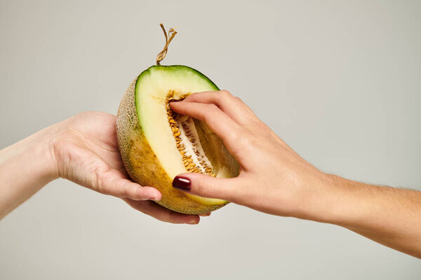 unknown woman with nail polish picking up seeds from fresh delicious cantaloupe on gray background