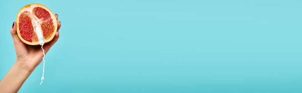 object photo of fresh grapefruit with tampon in it in hand of unknown woman on blue backdrop, banner