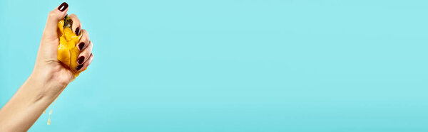 unknown woman squeezing delicious juicy persimmon in her hand on vibrant blue backdrop, banner