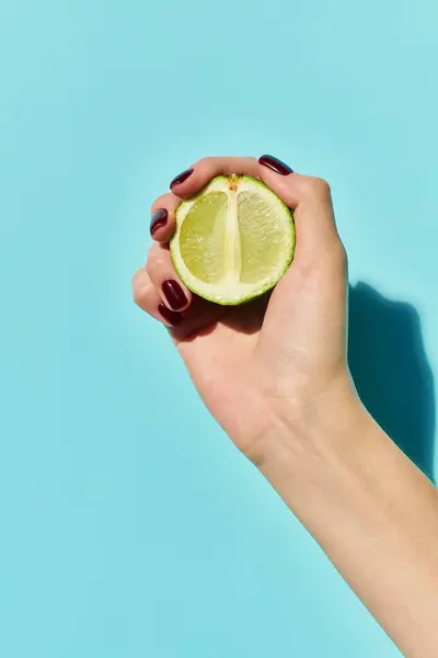 stock image fresh green lime in hand of unknown young woman with nail polish posing on vibrant blue backdrop