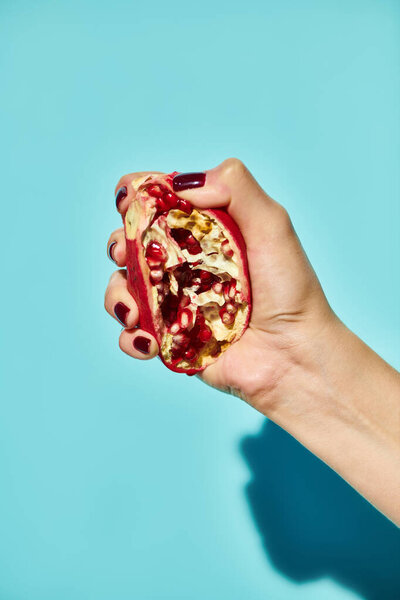unknown female model squeezing delicious pomegranate on blue vibrant background, object photo