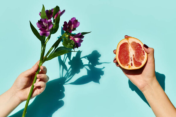 object photo of lilies and grapefruit in hands of unknown female model on blue vibrant background