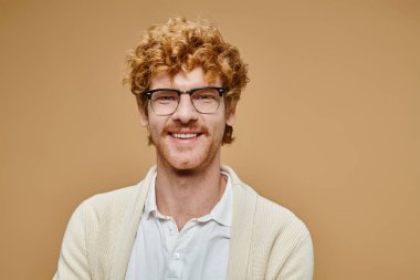 portrait of cheerful redhead man in eyeglasses and trendy light-colored clothes on beige backdrop clipart