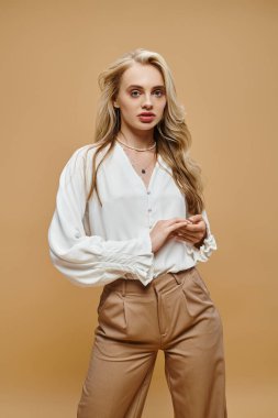 Klasik tarz gündelik giysiler içinde genç sarışın kadın bej renkli, zamansız moda kamerasına bakıyor.