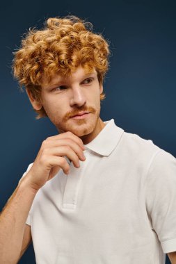 Beyaz polo tişörtlü, moda kızıl saçlı adamın portresi mavi, eski para modasına bakıyor.