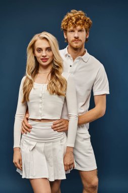 Eski moda kıyafetler içinde genç ve zarif bir çift mavi arka planda kameraya bakıyor, zamansız moda.