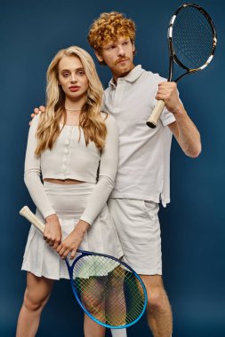 Sarışın kadın ve beyaz elbiseli kızıl saçlı adam. Mavi tenis raketleri, eski para tarzı.