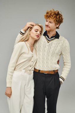 Gri elbiseli, zarif, kızıl saçlı bir adam. Gri elbiseli, genç ve şık bir kadının saçlarına dokunuyor.