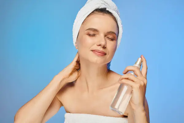 stock image smiling woman with radiant skin and closed eyes holding bottle of body spray on blue backdrop
