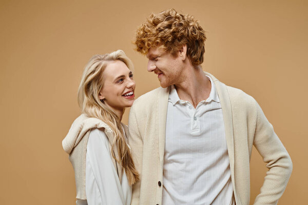 довольные блондинка и рыжеволосый мужчина в старом денежном стиле наряд глядя друг на друга на бежевый