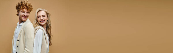 happy young couple in light-colored stylish attire posing back to back on beige backdrop, banner