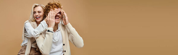 беззаботная блондинка, прикрывающая глаза модного рыжеволосого мужчины на бежевом, старом стиле денег, баннер