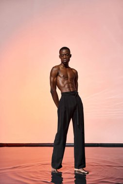 Kırmızı ışıklarla çevrili siyah şık pantolonlar giyen Afro-Amerikan bir adam.