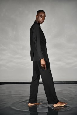 charming african american man in unbuttoned black suit posing alluringly and looking at camera clipart