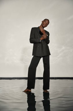 Siyahi seksi takım elbiseli Afrikalı Amerikalı çekici bir şekilde gri sulu arka planda poz veriyor.