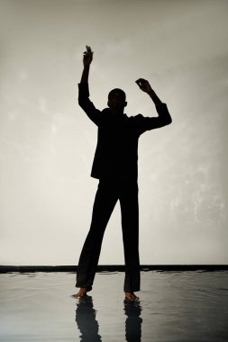 Gri sularda gölgelerde çıplak ayakla poz veren modaya uygun Afrikalı Amerikalı adamın silüeti.