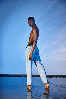 Mavi kotlu yakışıklı Afro-Amerikalı adam sulu arka planda kameraya bakıyor.