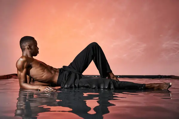 穿着湿裤子的漂亮性感的非洲男人躺在水面上 灯火通明 — 图库照片