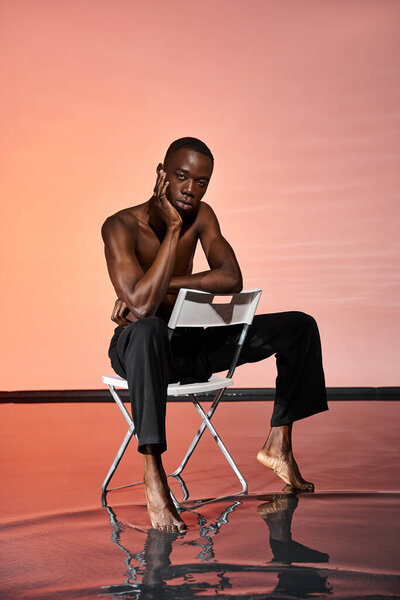 attractive sexy african american man sitting shirtless on chair and looking at camera, red lights