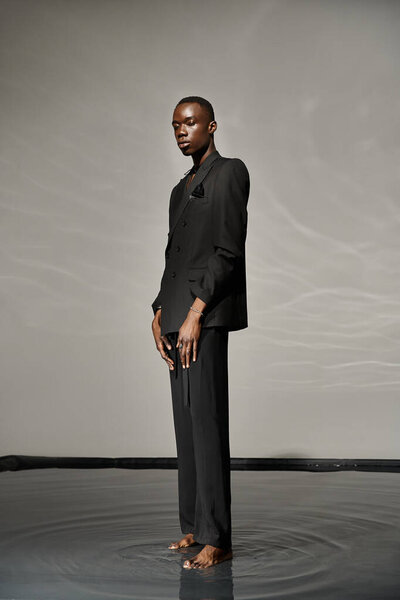 handsome stylish african american man in sexy unbuttoned suit posing on gray watery background