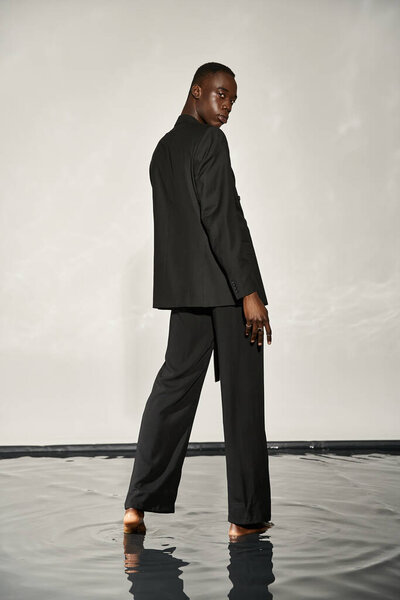 appealing african american man in black sexy suit posing attractively on gray watery background