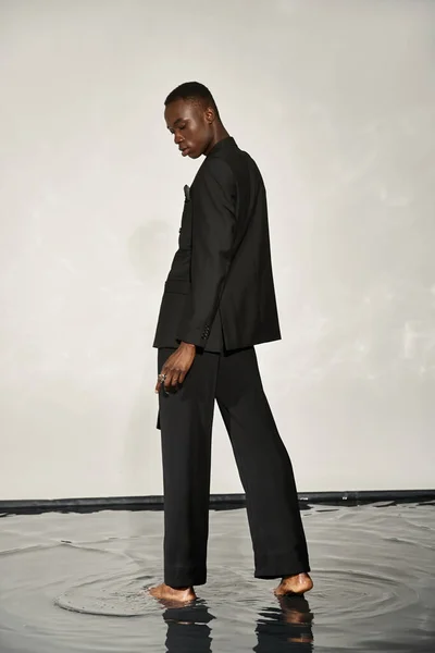 見栄えの良いアフリカ系アメリカ人男性 スタイリッシュな黒いスーツで水の背景に魅了 — ストック写真