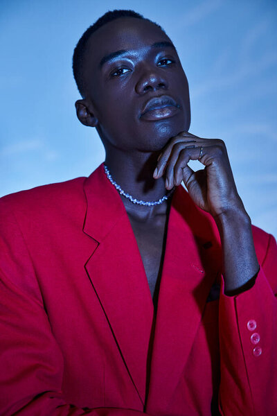 Attractive young african american man in red vibrant blazer posing on blue watery background