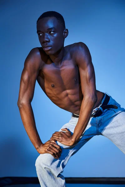 青い水色の背景にポーズするスタイリッシュなジーンズでトレンディなアフリカ系アメリカ人男性 — ストック写真