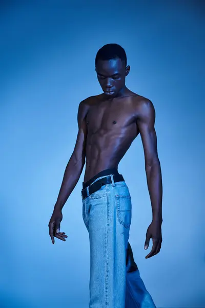 青い水色の背景にポーズするトレンディなジーンズの若いアフリカ系アメリカ人男性 — ストック写真