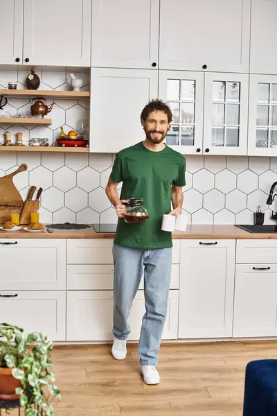 カジュアルなホームウェアのハンサムな陽気な男は キッチンでコーヒーを保持し カメラで微笑んでいる — ストック写真