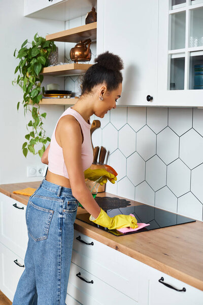 beautiful cheerful african american woman in cozy homewear washing her stove during spring cleaning