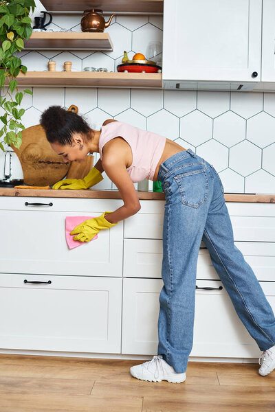 good looking young african american woman in comfy homewear washing kitchen, spring cleaning