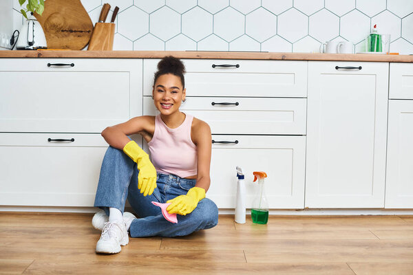 cheerful good looking african american woman in casual outfit sitting on floor and smiling at camera