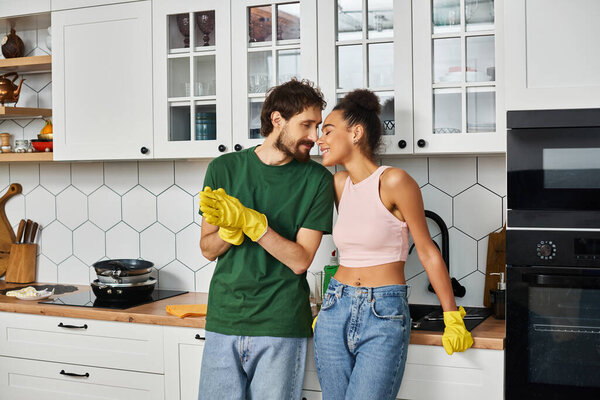 attractive joyous interracial couple in homewear enjoying each other during spring cleaning