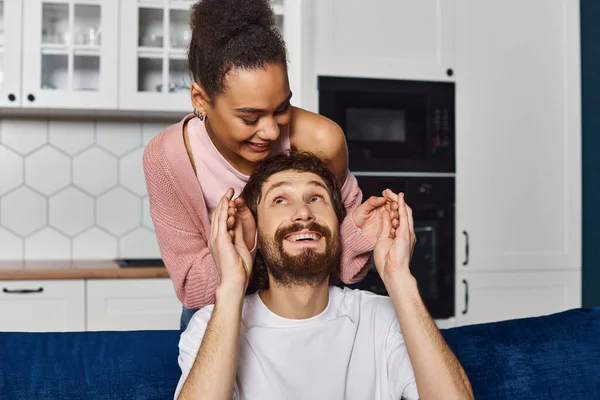 stock image handsome man looking at his african american girlfriend after she surprised him and closed eyes