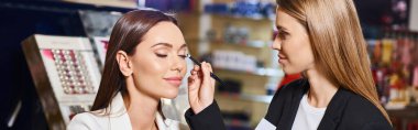 alluring shop assistant in black blazer applying eyeliner on her customer while in store, banner clipart