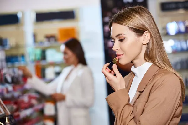 stock image beautiful blonde customer choosing lipstick with her blurred friend on background in cosmetics store