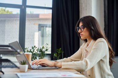 Bir iş kadını masa başında oturuyor, dizüstü bilgisayarına odaklanmış, bayilikle ilgili ürünlerle dolu modern bir ofis ortamında..