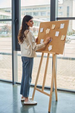 Bir iş kadını post-it 'lerle kaplı bir kurulun yanında durur, modern bir ofiste bayilik kavramları oluşturur..