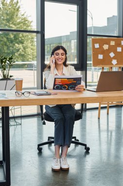 Modern ofis ortamında çizelgelerle masada oturan odaklanmış bir iş kadını iş ve öğrenme kavramını somutlaştırıyor..