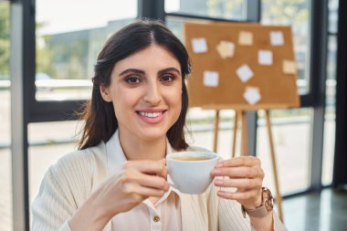 A businesswoman enjoys a peaceful moment at a table, sipping coffee in a modern office space with a franchise concept. clipart