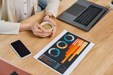 A businesswoman sitting at a table, deep in thought, with a cup of coffee in a modern office workspace. clipart