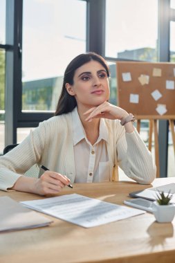 Odaklanmış bir iş kadını elinde kalemle modern bir ofis masasında oturuyor. Bayilik konseptine dalmış..