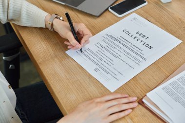 Masada oturan bir iş kadını, kalem ve kağıtla notlar yazmaya odaklanmış, modern ofis ortamında beyin fırtınası yapan bir iş kadını..