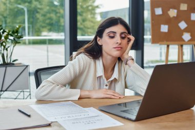 Modern bir ofiste masa başında oturan bir iş kadını laptopuna odaklanmış, gelişmekte olan bir bayilik kavramını somutlaştırıyor..